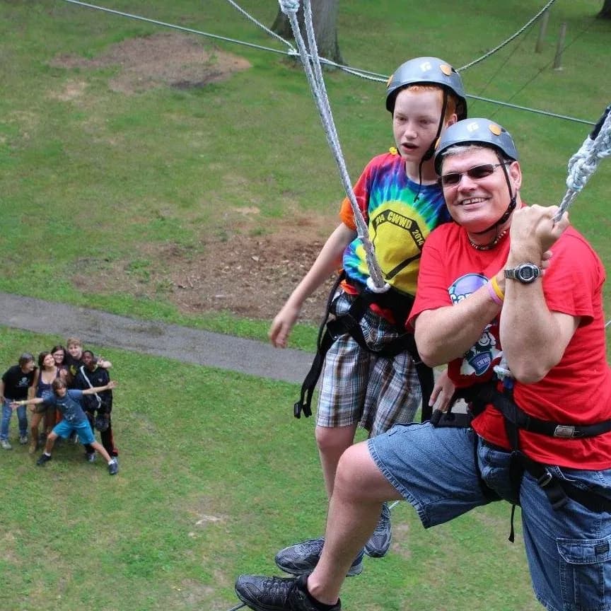 Young Henri on the ropes course at camp with a counselor